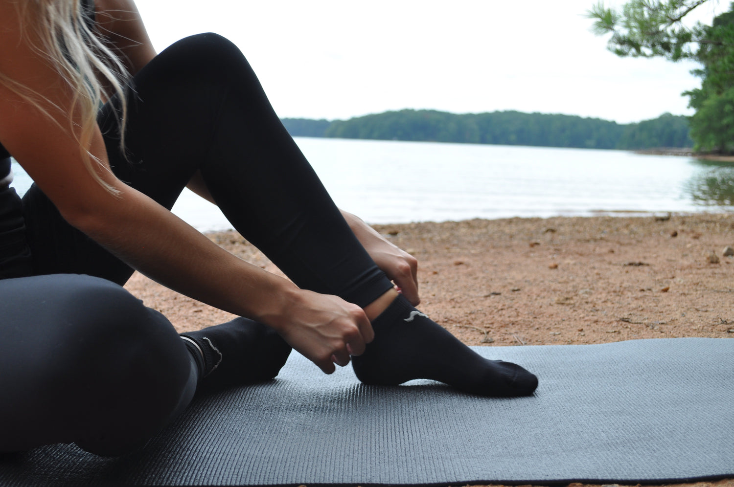 Image of a girl on a yoga mat wearing our odorless socks, practicing yoga in a serene lakeside setting